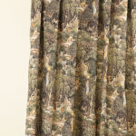 Tessuto decorativo ispirato a scene esotiche, raffigurante donne in abiti tradizionali immerse in una lussureggiante foresta tropicale con cascate, alberi imponenti e vegetazione rigogliosa. I toni caldi del verde, marrone e ocra creano un design ricco e suggestivo, ideale per arredamenti etnici, tende, cuscini e decorazioni d'interni in stile tropicale.