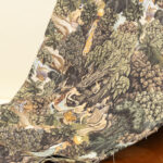 Tessuto decorativo ispirato a scene esotiche, raffigurante donne in abiti tradizionali immerse in una lussureggiante foresta tropicale con cascate, alberi imponenti e vegetazione rigogliosa. I toni caldi del verde, marrone e ocra creano un design ricco e suggestivo, ideale per arredamenti etnici, tende, cuscini e decorazioni d'interni in stile tropicale.