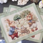 Tovaglietta pasquale in tessuto Gobelin con illustrazione di coniglietti vestiti in abiti vintage, ambientata in un giardino primaverile con alberi in fiore e un carretto pieno di uova decorate. Il bordo verde aggiunge un tocco raffinato, perfetto per decorare la tavola di Pasqua con stile e originalità.