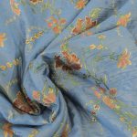 Lampasso fabric with light blue background and woven floral pattern in classic style. Flowers in shades of red, orange and yellow with green leaves, perfect for curtains, pillows, upholstery and shabby chic decorations. Elegant and vibrant print for decorating with personality. Made in Italy.
