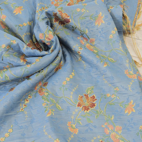 Lampasso fabric with light blue background and woven floral pattern in classic style. Flowers in shades of red, orange and yellow with green leaves, perfect for curtains, pillows, upholstery and shabby chic decorations. Elegant and vibrant print for decorating with personality. Made in Italy.