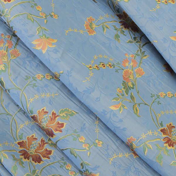Lampasso fabric with light blue background and woven floral pattern in classic style. Flowers in shades of red, orange and yellow with green leaves, perfect for curtains, pillows, upholstery and shabby chic decorations. Elegant and vibrant print for decorating with personality. Made in Italy.