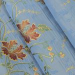 Lampasso fabric with light blue background and woven floral pattern in classic style. Flowers in shades of red, orange and yellow with green leaves, perfect for curtains, pillows, upholstery and shabby chic decorations. Elegant and vibrant print for decorating with personality. Made in Italy.