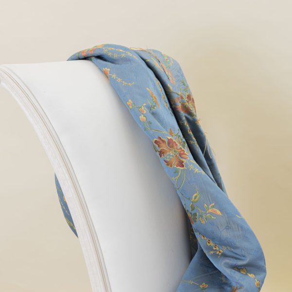 Lampasso fabric with light blue background and woven floral pattern in classic style. Flowers in shades of red, orange and yellow with green leaves, perfect for curtains, pillows, upholstery and shabby chic decorations. Elegant and vibrant print for decorating with personality. Made in Italy.