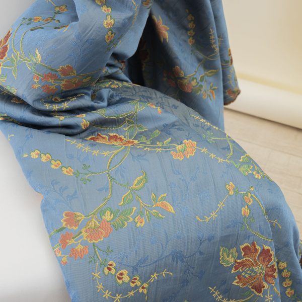 Lampasso fabric with light blue background and woven floral pattern in classic style. Flowers in shades of red, orange and yellow with green leaves, perfect for curtains, pillows, upholstery and shabby chic decorations. Elegant and vibrant print for decorating with personality. Made in Italy.
