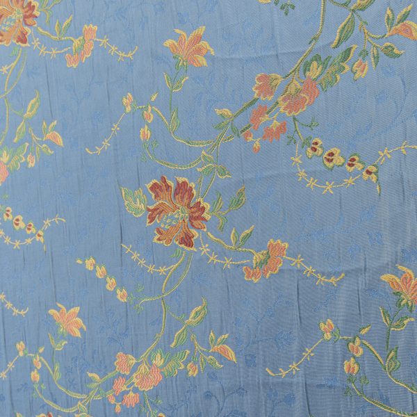 Lampasso fabric with light blue background and woven floral pattern in classic style. Flowers in shades of red, orange and yellow with green leaves, perfect for curtains, pillows, upholstery and shabby chic decorations. Elegant and vibrant print for decorating with personality. Made in Italy.