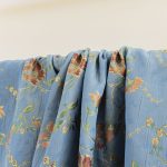 Lampasso fabric with light blue background and woven floral pattern in classic style. Flowers in shades of red, orange and yellow with green leaves, perfect for curtains, pillows, upholstery and shabby chic decorations. Elegant and vibrant print for decorating with personality. Made in Italy.